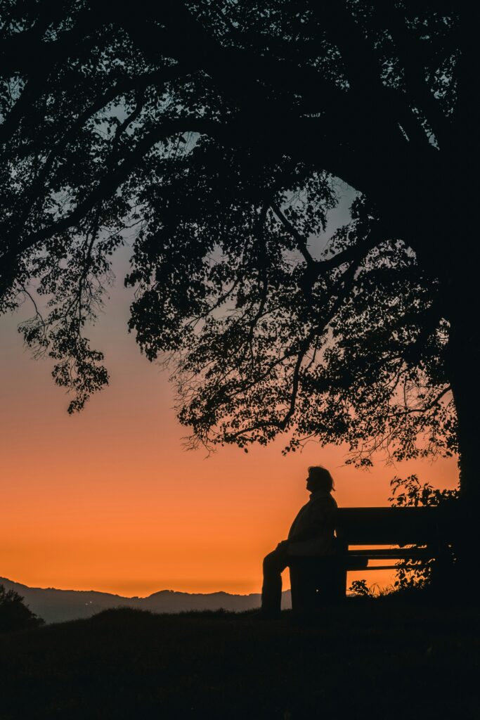 An elderly woman sitting peacefully by a tree, exuding a sense of serenity and calm, symbolizing peace of mind